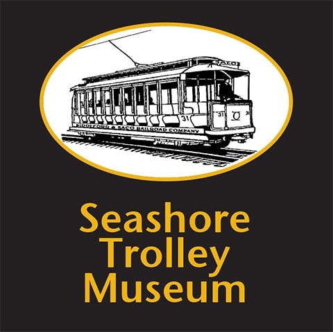 A black and white drawing of a vintage trolley car inside a yellow oval, above the text Seashore Trolley Museum in yellow on a black background.
